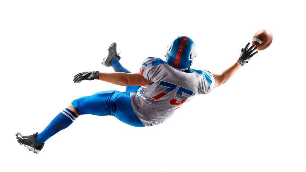 A college wide receiver stretching out to grab a ball, against a white background.