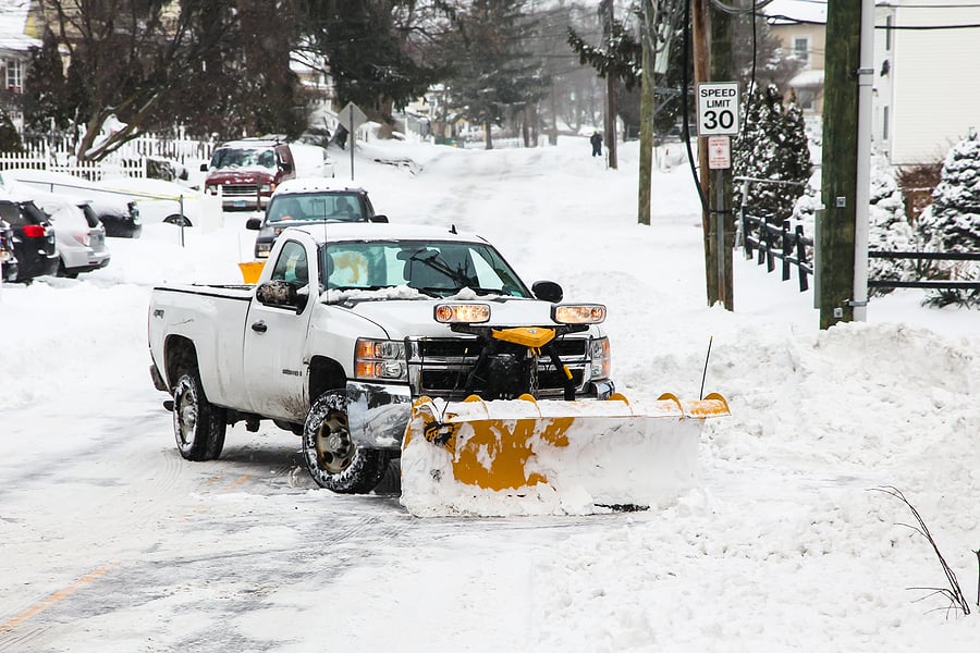 A white pickup truck plowing snow on suburban street