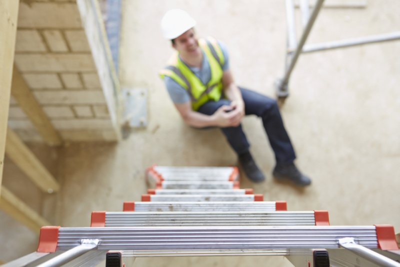 contractor with public liability insurance sits at bottom of ladder clutching leg in pain after injury
