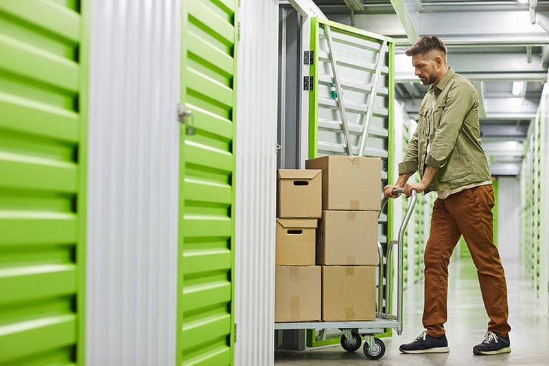 Man pushing a cart loaded with boxes into a storage unit