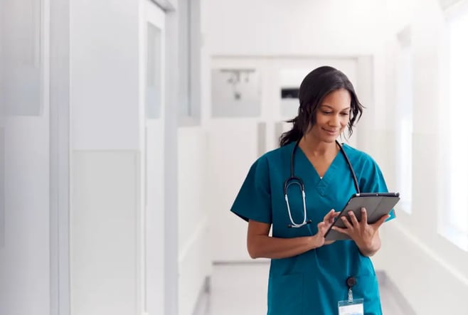 Female doctor walks down hallway smiling and staring at clipboard