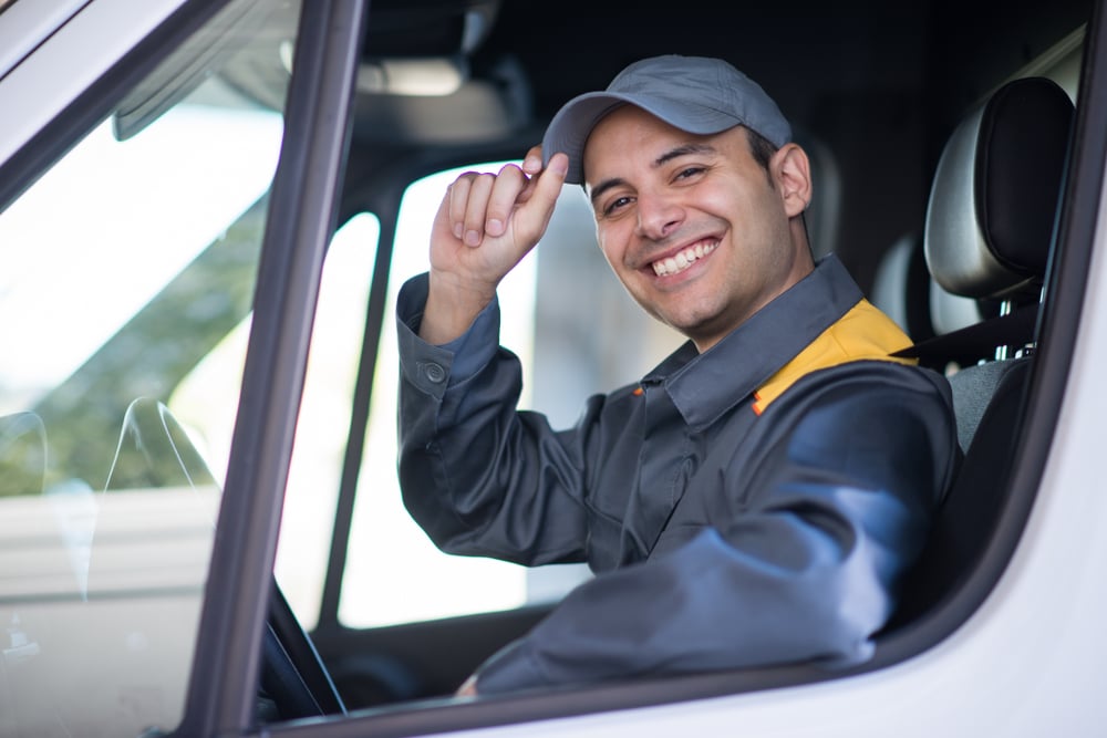 Delivery driver tips hat and smiles at camera from truck