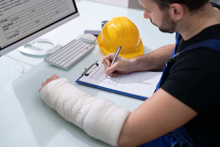 Injured contractor sits at a desk filling out contractor liability insurance papers